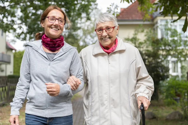 Zwei ältere Menschen gehen gemeinsam Arm in Arm durch das Grüne.